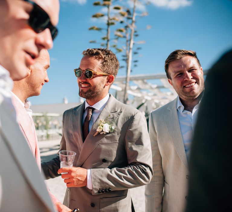 The groom greeting guests in the sun wearing sunglasses and a Thom Sweeney suit