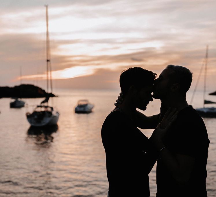 Sun sets behind grooms as they kiss in Ibiza 