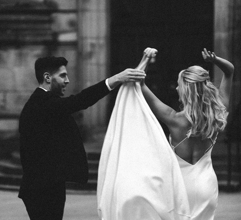 Black and white portrait of the groom twirling his bride in a slip wedding dress 