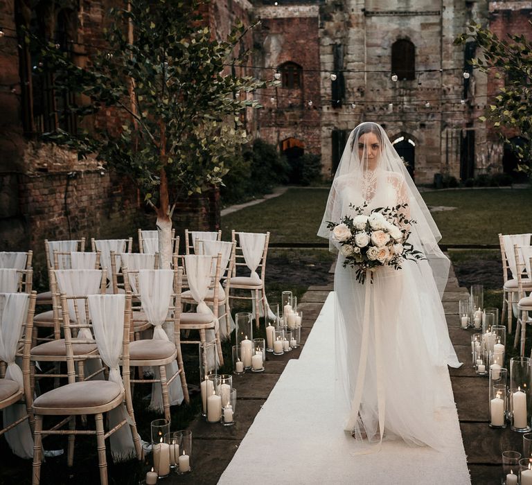 Bride walking down the aisle wearing a wedding veil and holding a rose bouquet 