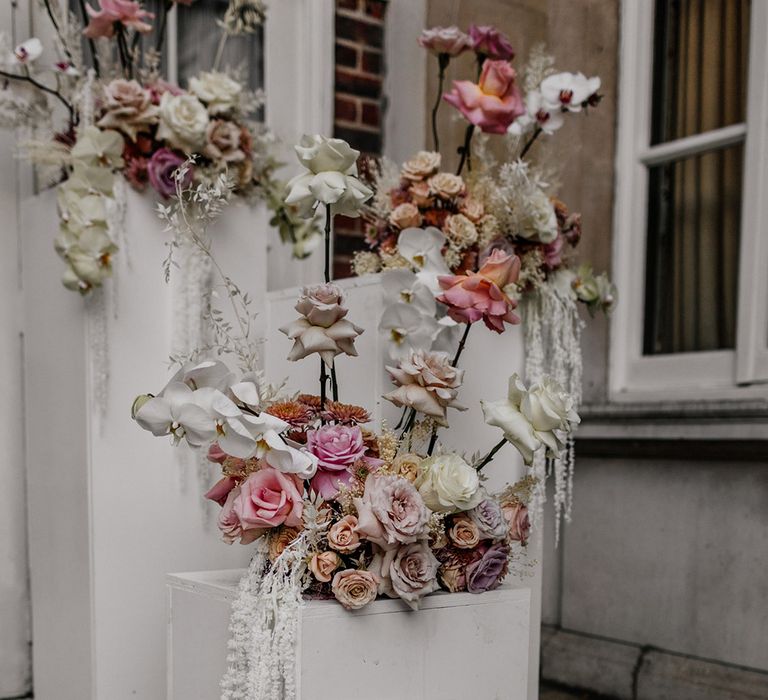 Frosted acrylic wedding welcome sign resting against a white plinth decorated with romantic blush wedding flowers 