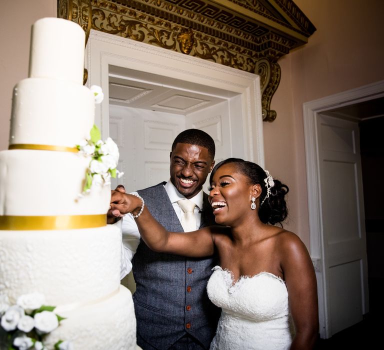 Bride & groom cut four-tier wedding cake with gold trim