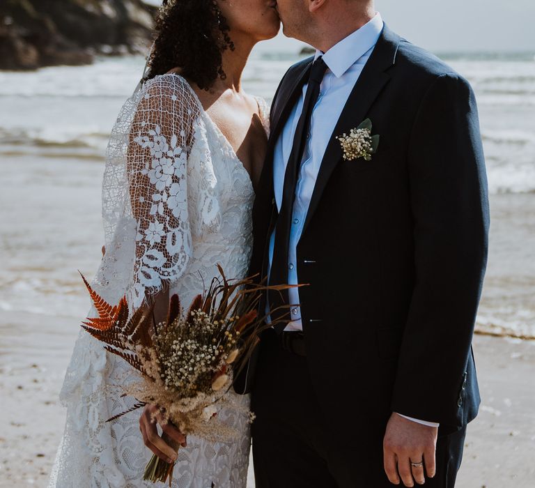 Bride & groom kiss as they stand on the beach with the sea in the background 