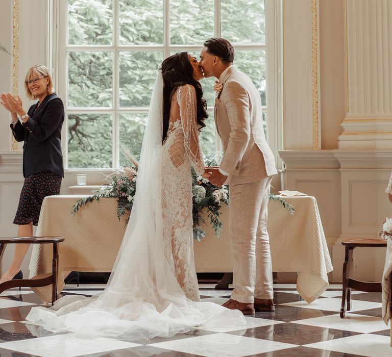 Bride & groom kiss in front of large window on their wedding day