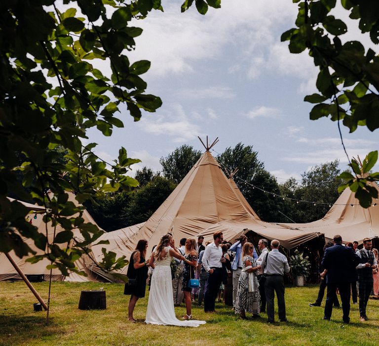 Outdoor tipi with wedding guests stood outdoors in the sunshine 