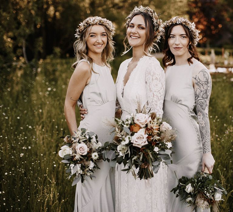 Boho bride at outdoor meadow wedding with her bridesmaids in grey satin dresses and dried flower crowns 