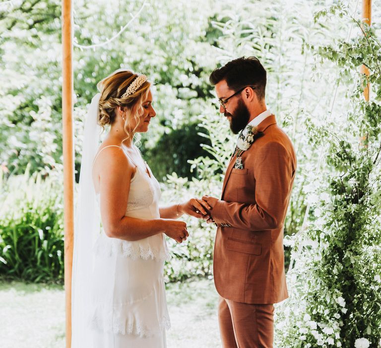 Bride & groom hold hands during wedding ceremony on a bright and sunny day outdoors in Cornwall