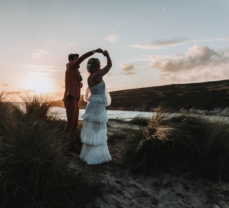 Groom spins his bride around on the beach on their wedding day as the sun goes down