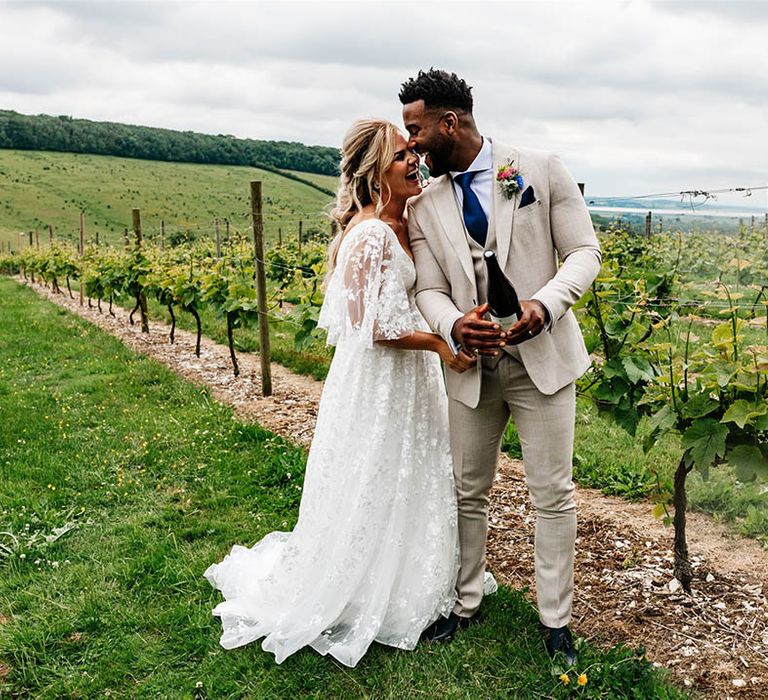 Bride in a lace wedding dress laughing with her husband in a beige check suit at Little Wold Vineyard 