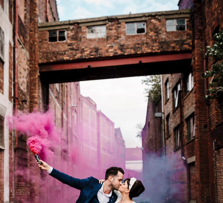 Liverpool micro wedding with bride in a trouser suit and turban headband and groom in a navy suit holding pink and blue smoke grenades