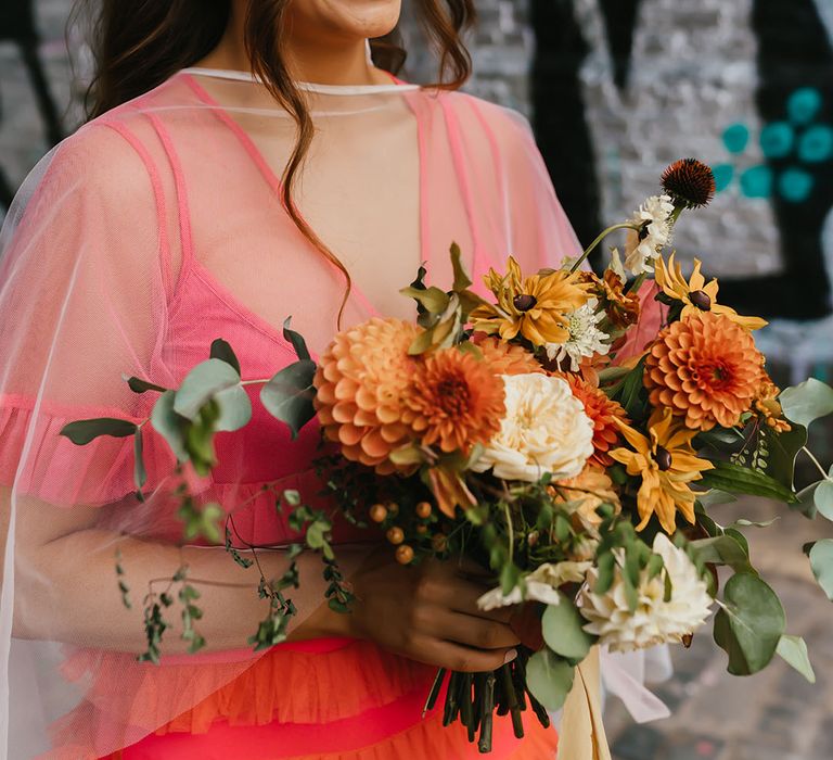 Beautiful bride with orange Frida Kahlo flower crown, brown eyeshadow and red lipstick holding her wildflower wedding bouquet 