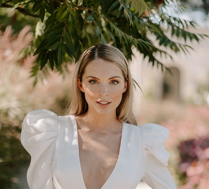 Blonde bride in a long sleeve bridal jumpsuit with sleek hair and natural wedding makeup 