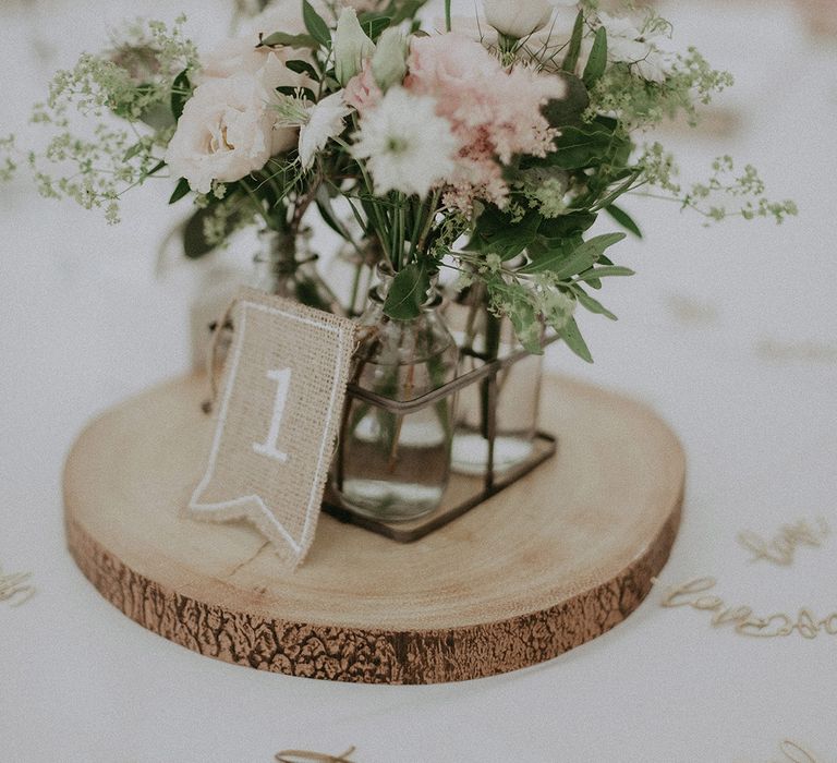 Rustic wedding table decor with tree slice, pink and white flowers in bottles and a burlap table number sign 