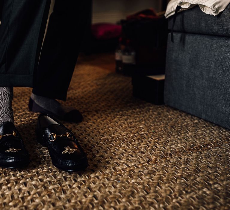 Groom in black and white patterned socks puts on leather loafers before Cornish wedding 