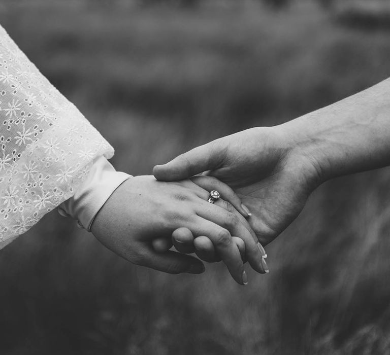 Black & white image of bride & groom holding hands as they walk through field on their wedding day