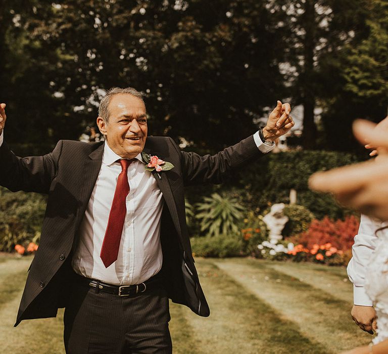 Father of the Bride celebrates as he walks across on lawn on wedding day