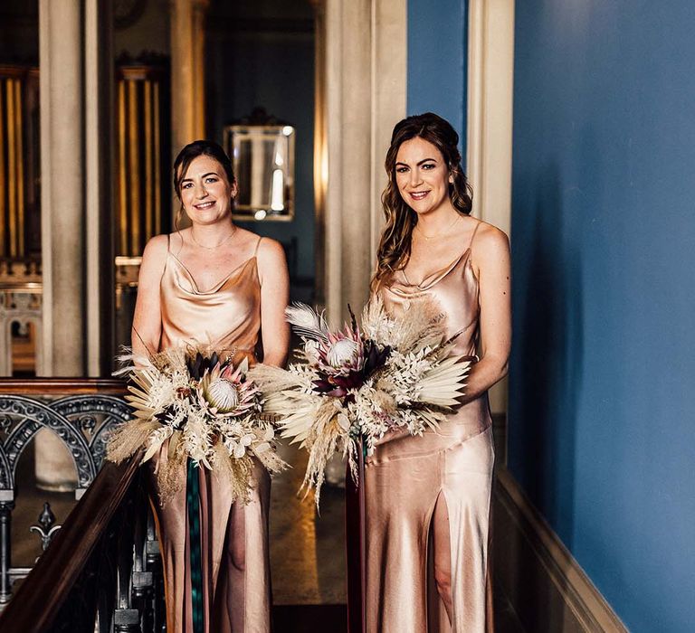 Bridesmaids wear silk bridesmaids gowns whilst holding floral bouquets