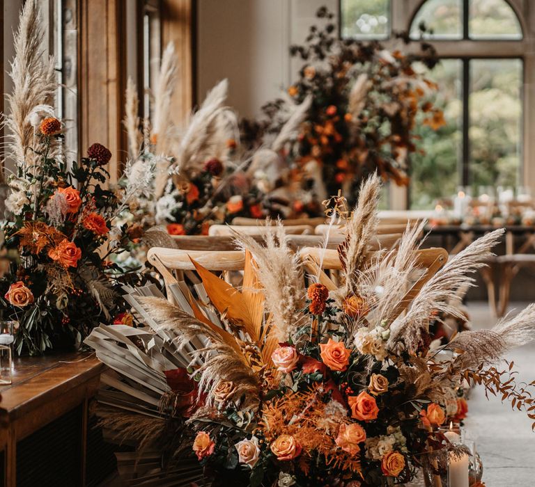 Mixed orange floral installations with roses and pampas grass in ceremony room with wooden chairs for intimate ceremony in Scotland 