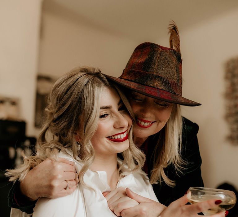 Wedding guest in a felt fedora embracing the bride on the wedding morning 