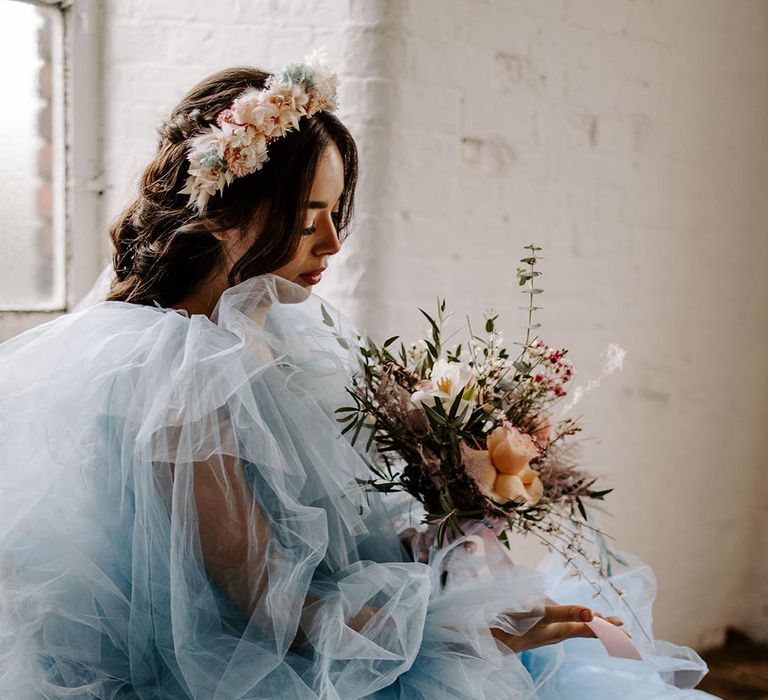 Bride in a blue tulle wedding dress holding a peach bouquet with a peach and beige dry flower hair accessory 