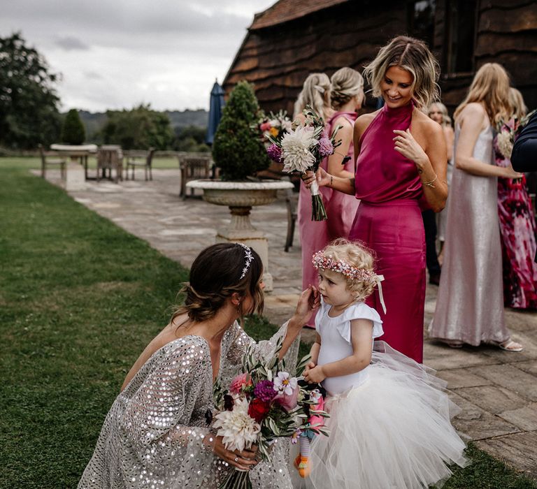 Bride in a silver wedding dress talking to her little flower girl in a tulle skirt 