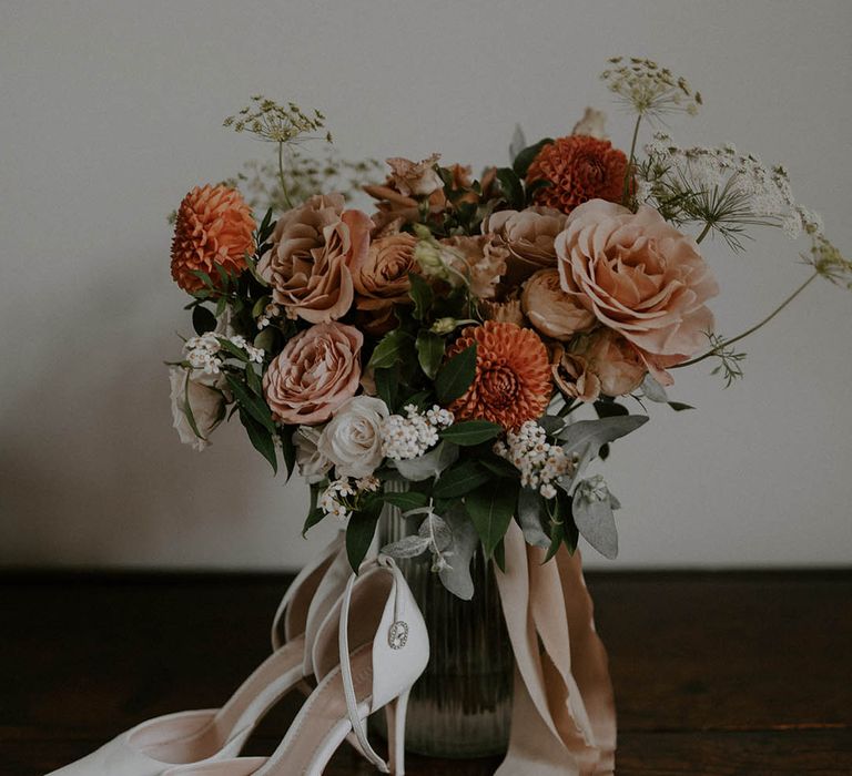 White wedding shoes with orange and blush wedding bouquet tied with pink ribbon