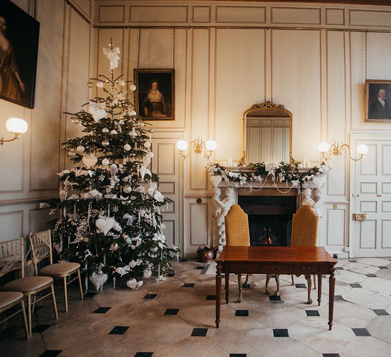 Christmas tree sits in the corner of grand room at Gosfield Hall complete with wreath across fireplace 