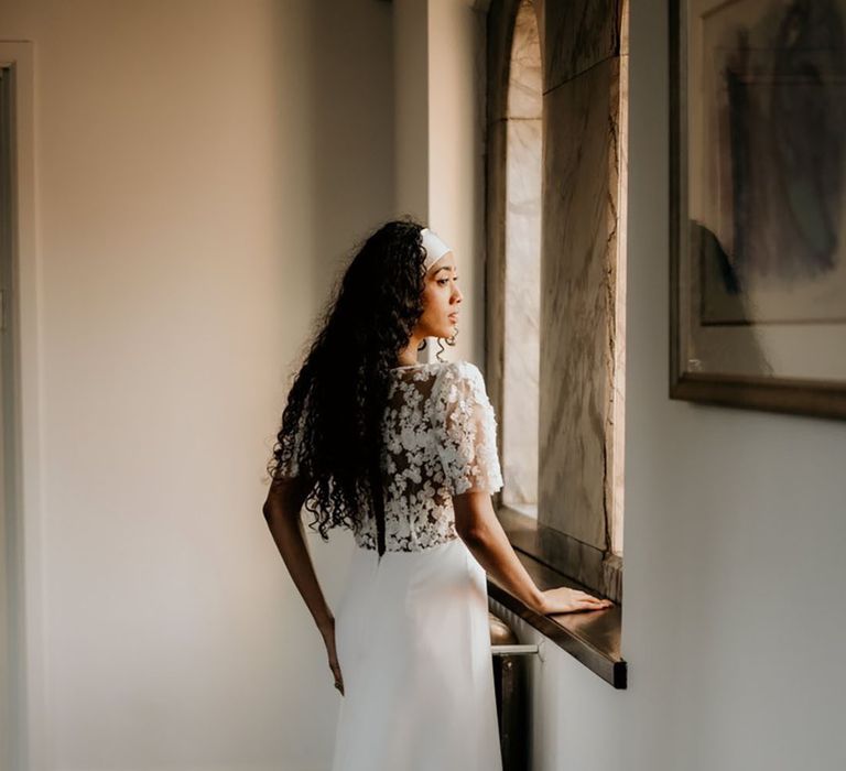 Black bride with long naturally curly hair wearing a Story Of My Dress Bridal wedding dress with lace bodice and minimalist skirt 