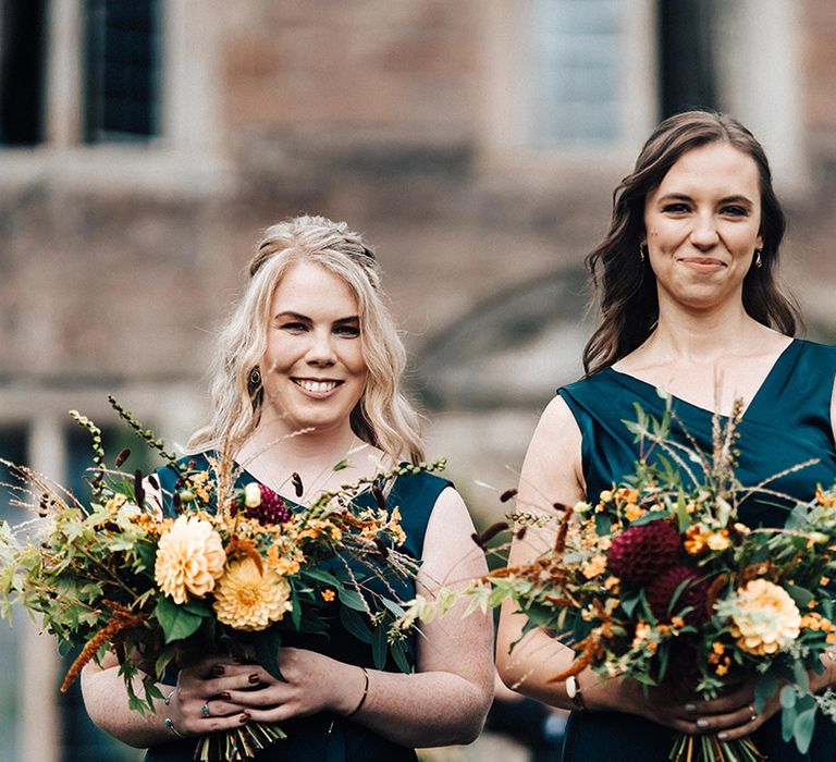 Bridesmaids in blue dresses smile at the camers holding yellow, orange and red bouquets