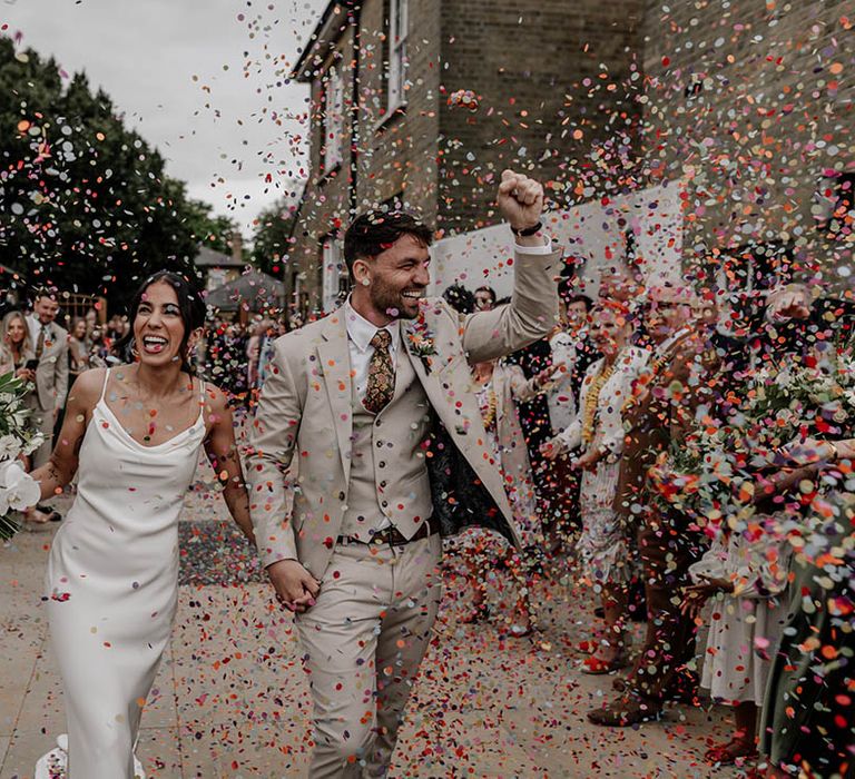 Colourful confetti photograph with bride in a slip wedding dress and groom in a stone three-piece suit with paisley tie 