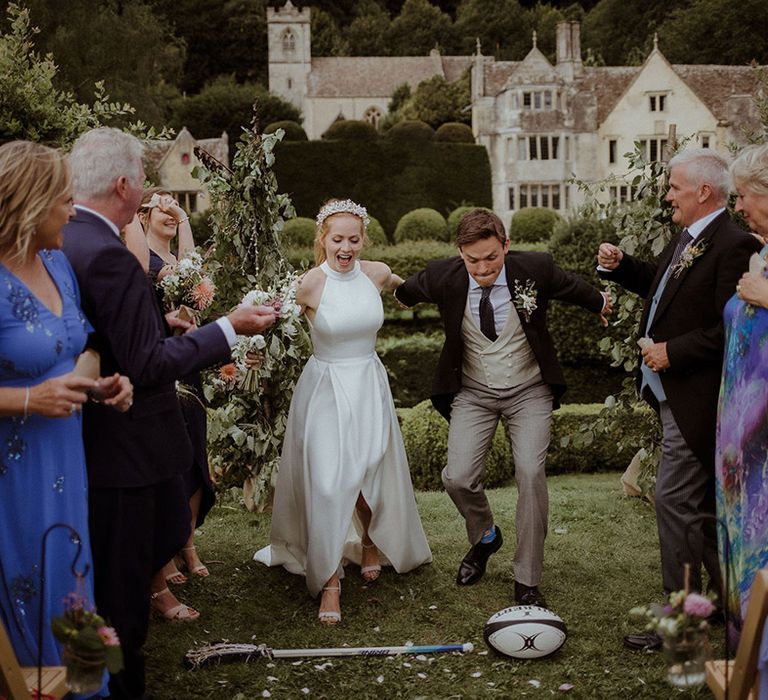 Bride and groom get ready to jump over a rugby ball and lacrosse stick 