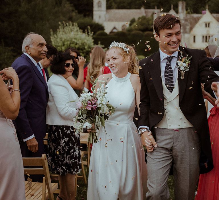 Smiling bride and groom walk back down the aisle through confetti after handfasting ceremony 