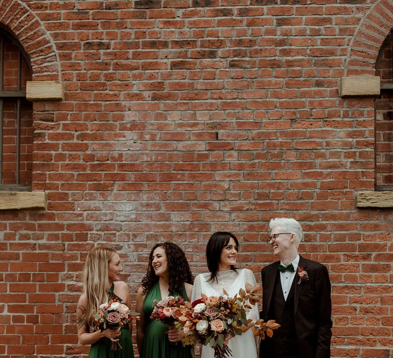 Bride stands with her bridesmaids who wear deep green gowns complete with halter neck styling and Man Of Honour who wears Hugo Boss suit