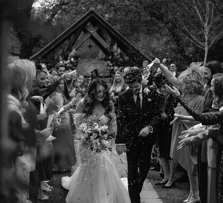 Bride in tulle wedding dress with groom exit their outdoor ceremony to confetti 