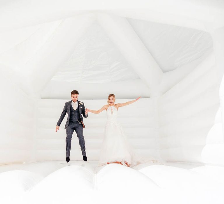 Bride and groom jump together on their white wedding bouncy castle 