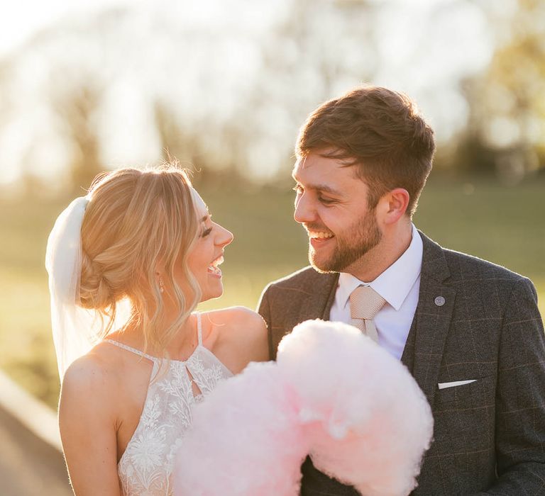 Bride and groom smile at each other as they hold candy floss 