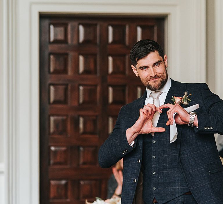 Wedding guest in blue three piece suit makes a love heart 