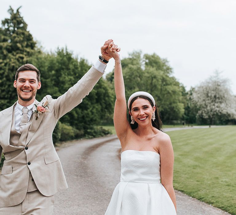 Bride and groom take couple portraits as they walk with their joint hands in the air 