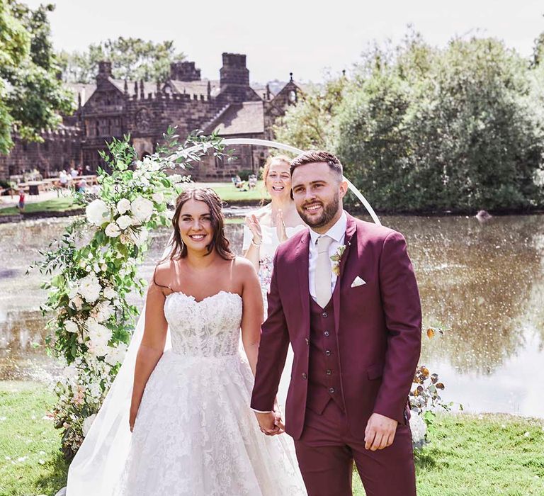 Outdoor wedding ceremony at East Riddlesden Hall with bride in a strapless lace wedding dress and groom in a burgundy coloured suit