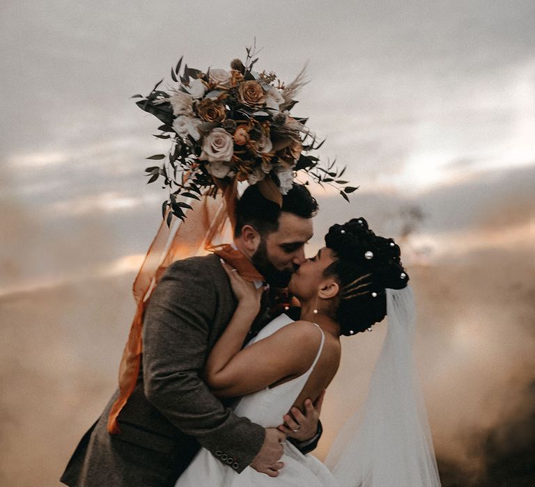 Bride & groom kiss outdoors during couples portraits with orange smoke bomb in the background