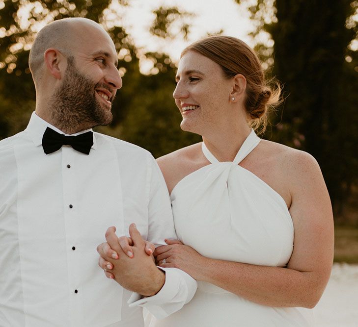 Bride wears her red hair pulled into low bun and looks lovingly at her groom in black tie 