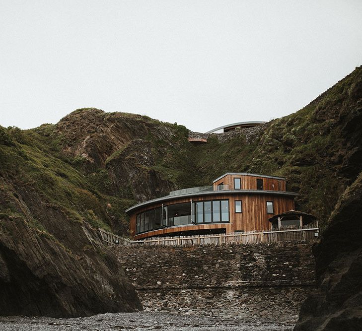 Wooden building with large glass windows sits between rocks at Tunnels Beach