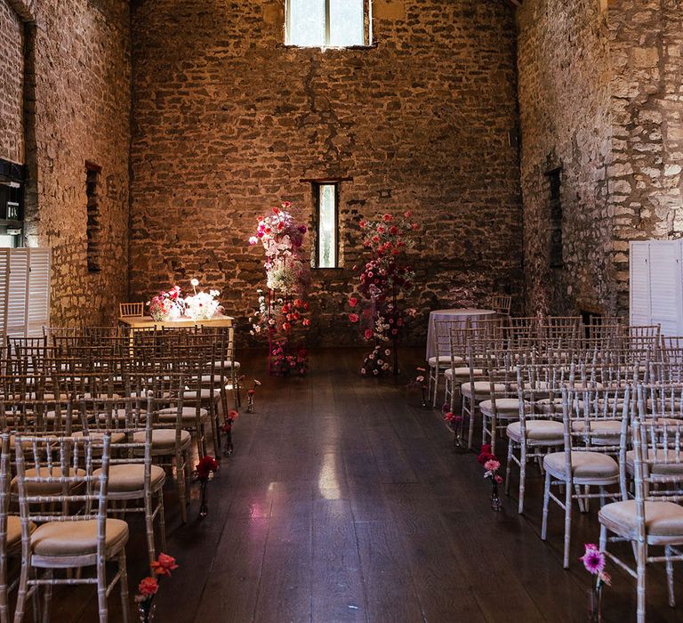 Bright pink floral arch at the end of aisle in front of exposed brick wall with rustic vibe at the Priston Mill wedding venue