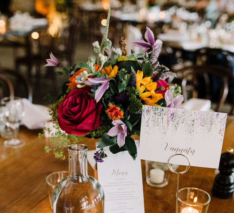 Bright floral centrepiece on wooden table complete with floral and white stationery 