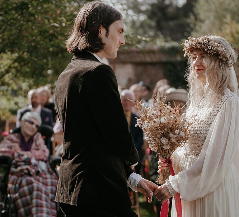 Blonde bride wears dried floral crown complete with dried floral bouquet as she marries her groom during Pagan wedding ceremony 