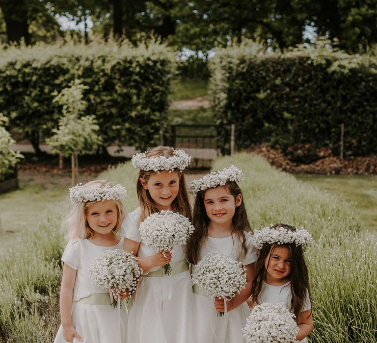 Flower girls in white dresses with a satin green belt holding bouquets of gypsophila and matching flower crowns 