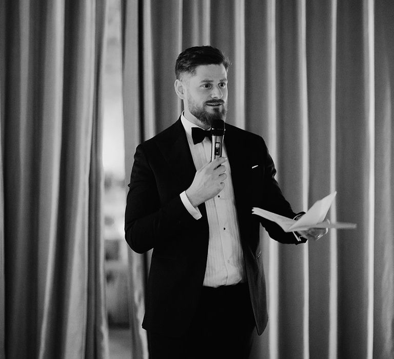 Groom stands holding a microphone as he reads out his wedding speech