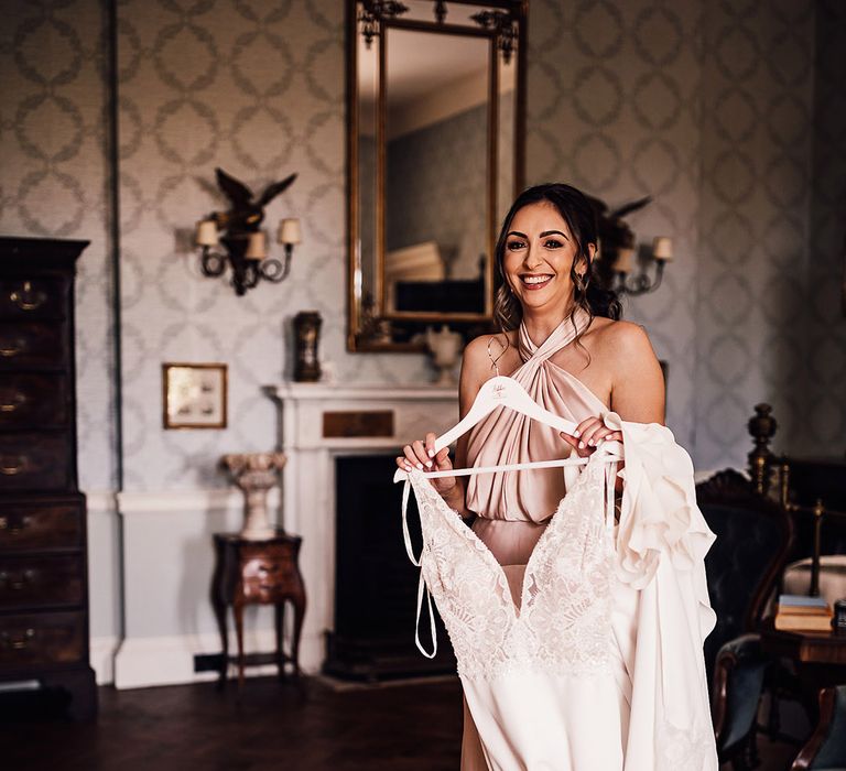 The bridesmaids in a halter neck pink satin dress holding the bride's dress to help her get ready 