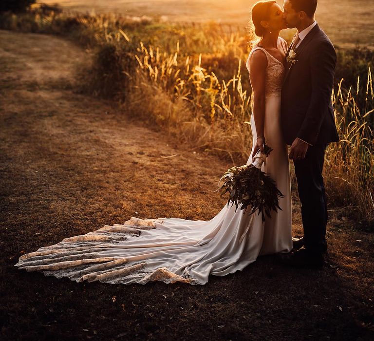 Gorgeous golden hour couple portrait of the bride and groom sharing a kiss on their wedding day