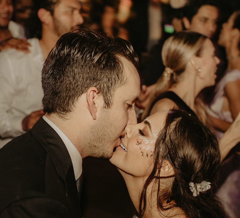 Bride with her face painted kisses her groom during rave wedding reception outdoors in the jungle 